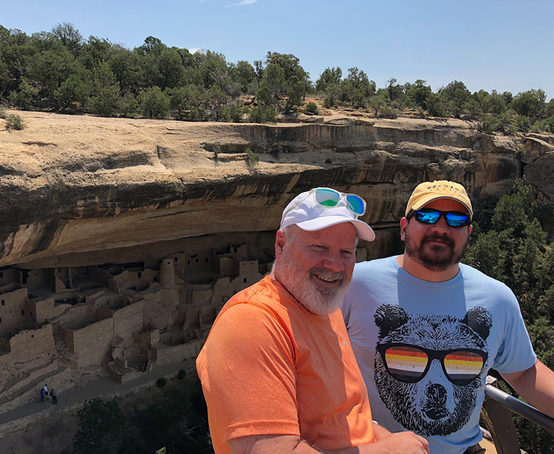 jerry and greg standing together with cliff dwellings in the background