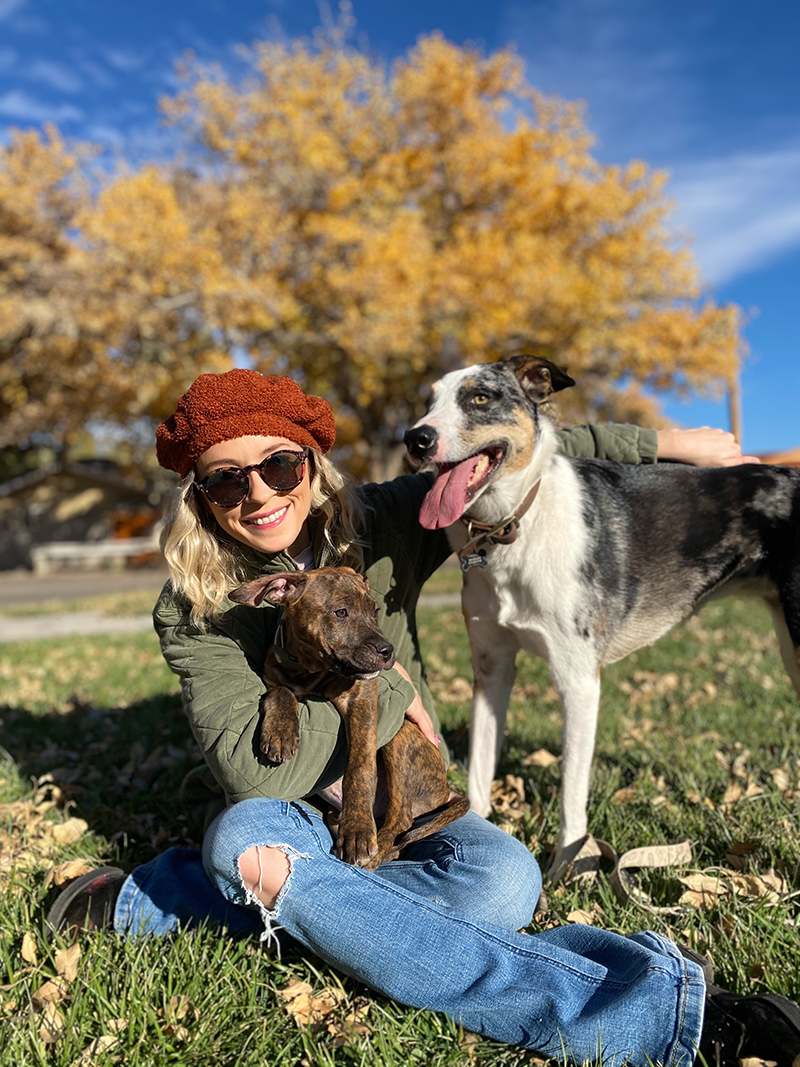 Taylor sitting in the grass with two dogs and an autumn tree in the background